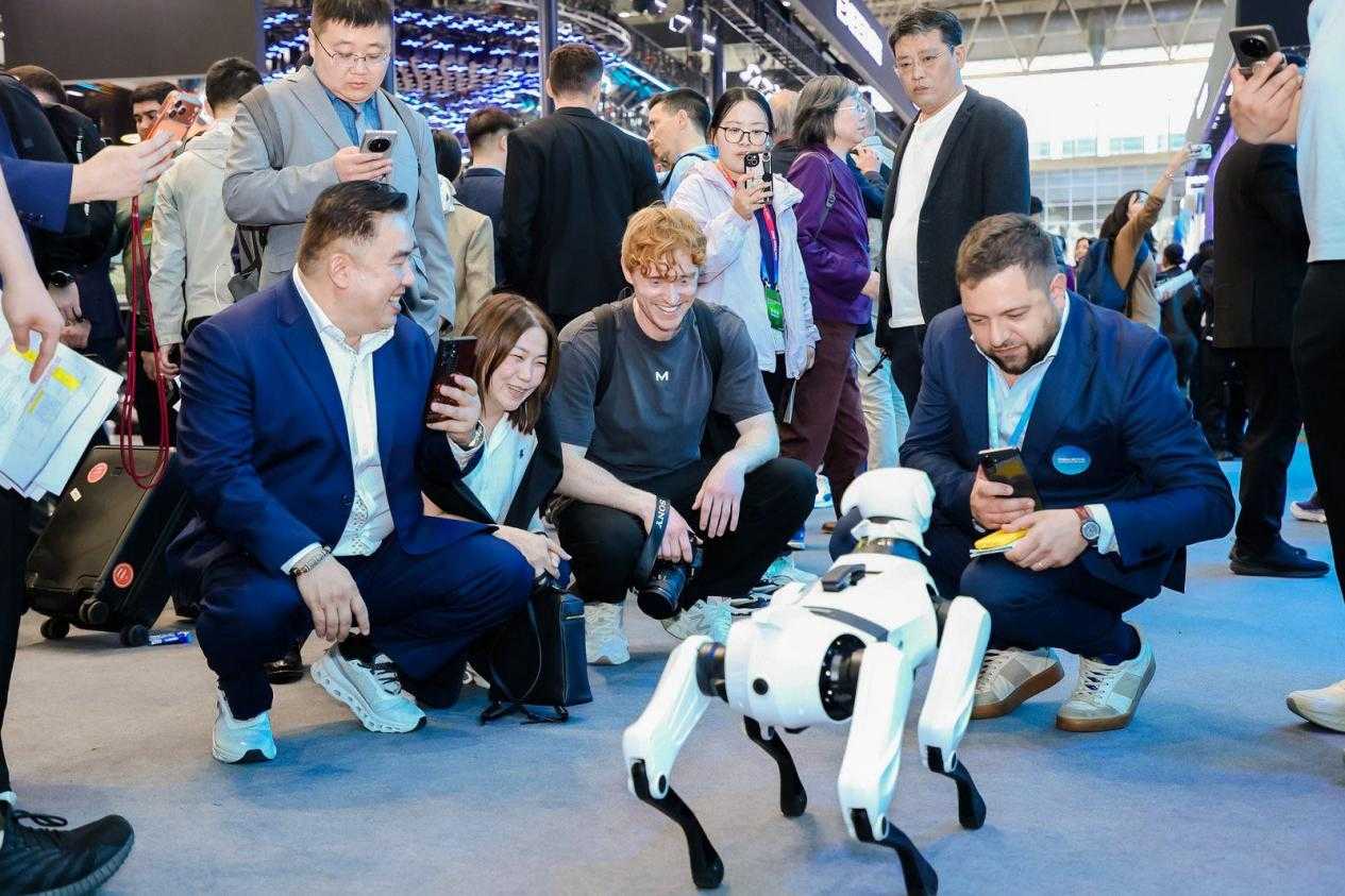 2026 Pekin Otomobil Fuarı'nda uluslararası ziyaretçilerin yoğun ilgi gösterdiği ve eğlenerek etkileşime girdiği, Chery'nin yenilikçi AiMOGA Robotics serisine ait robot köpek.